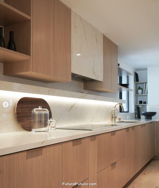 Futuro Futuro 36 inch Slide insert range hood hidden behind marble cladding above a black glass cooktop in a Santa Monica kitchen with light wood cabinets, veined marble backsplash, and warm LED lighting.