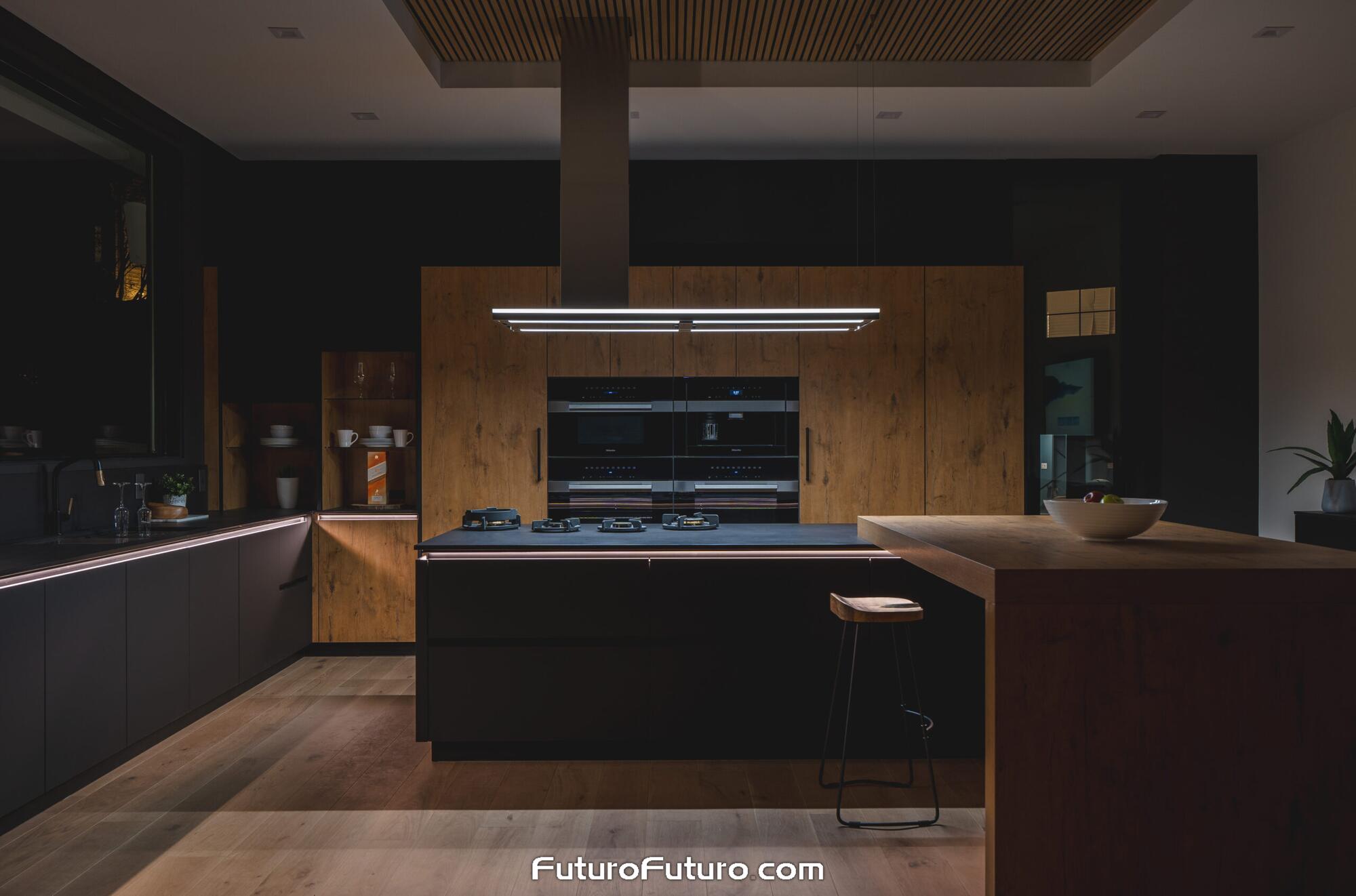 Dark finish Futuro Futuro 69 inch Streamline island range hood with LED canopy lights over a charcoal cooktop island in an Arlington VA kitchen featuring warm wood wall ovens and light hardwood floors.